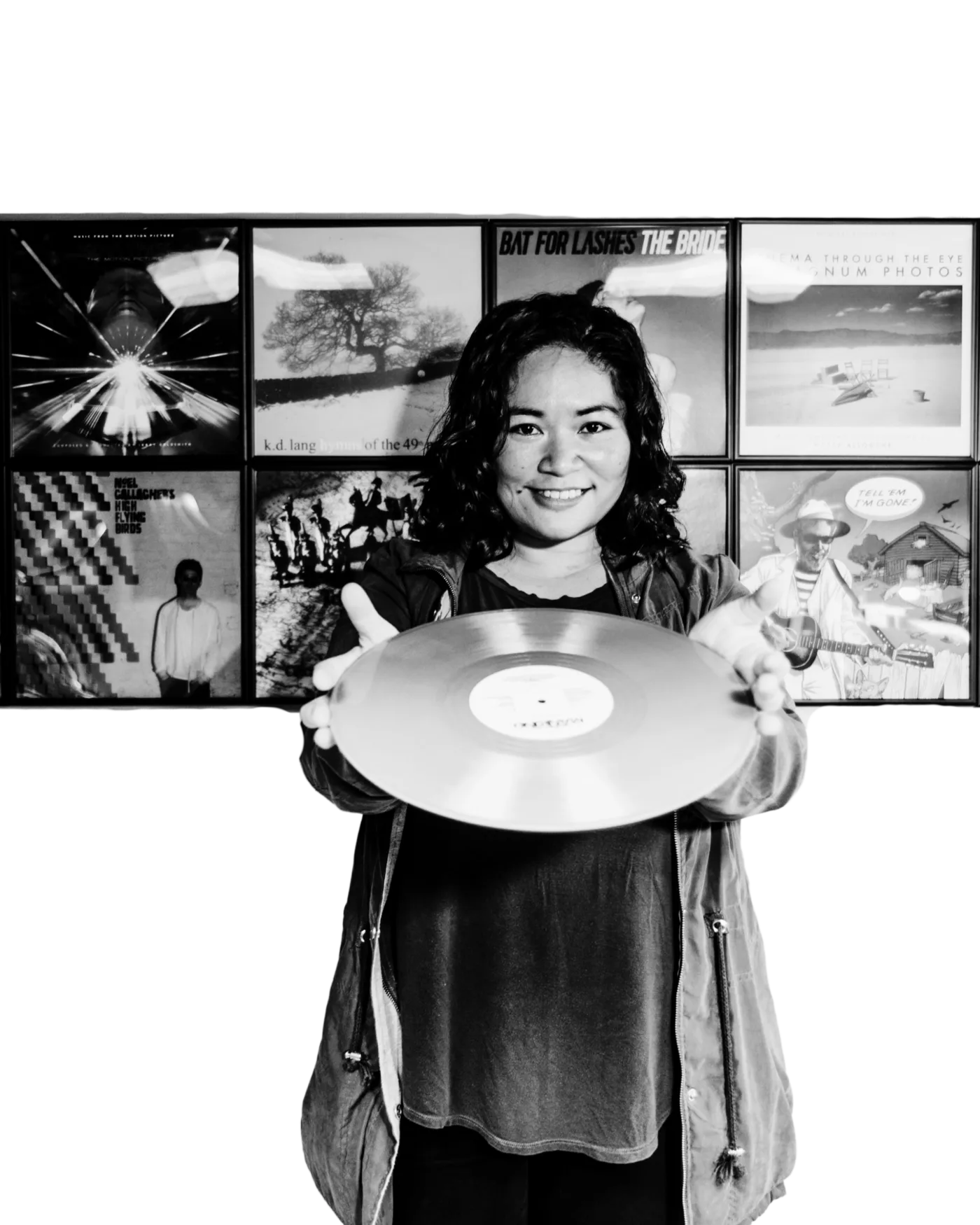 Jett Galindo smiling and holding a vinyl record in front of a wall of framed album covers