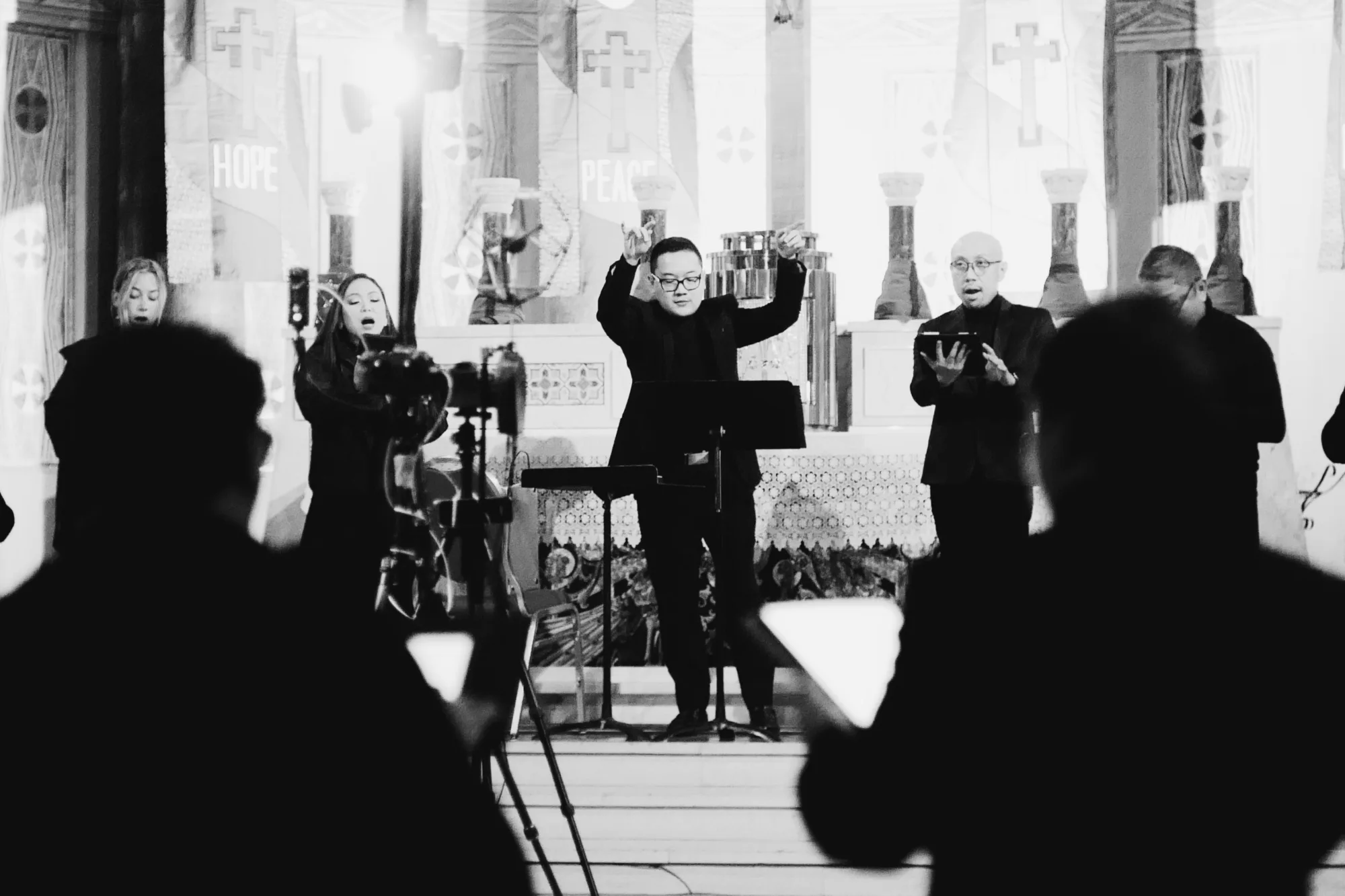 A vocal ensemble performing in a church, conductor mid-gesture, recording microphones in the foreground