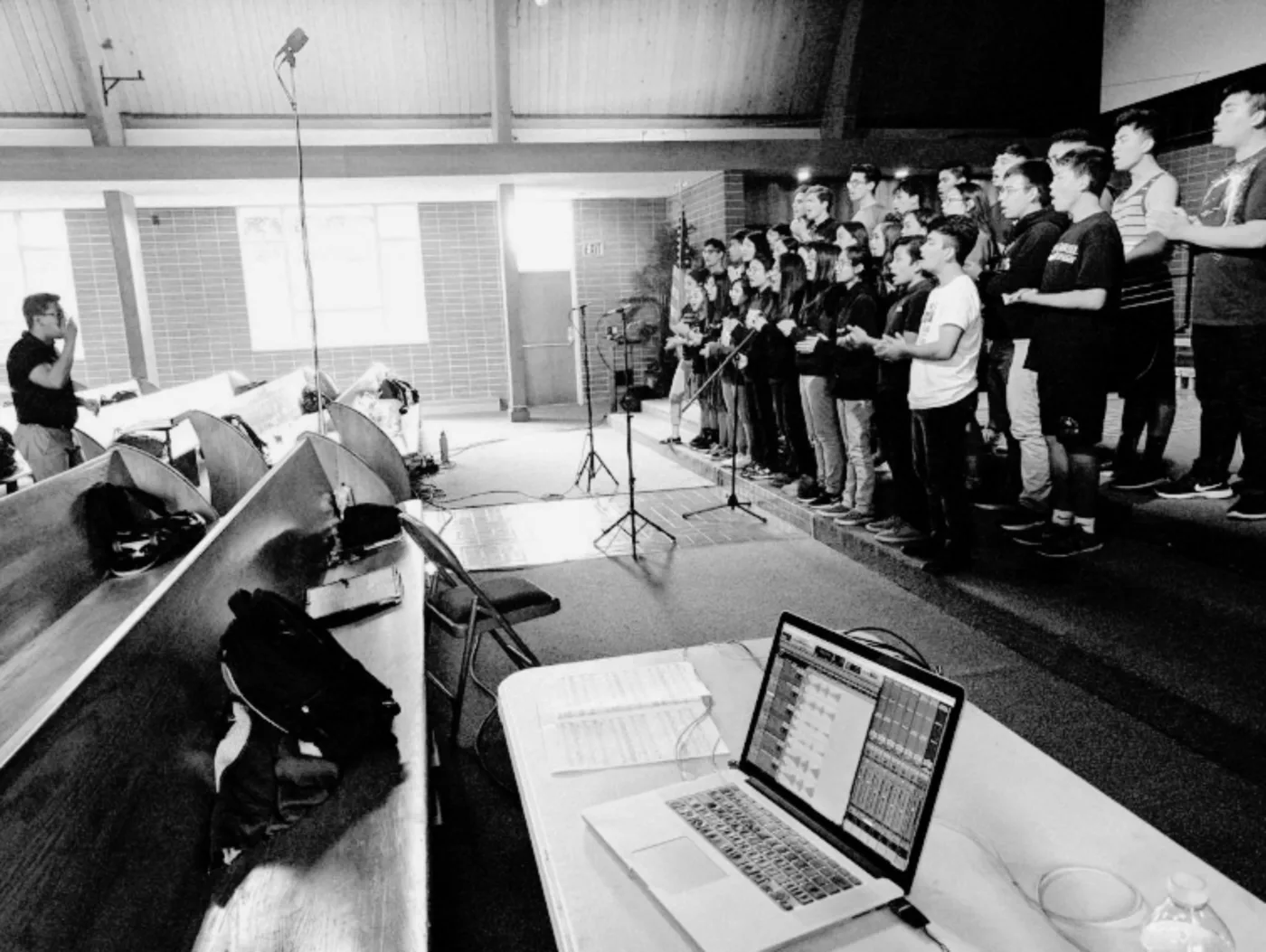 A choir performing on risers while a recording laptop and microphones capture the session
